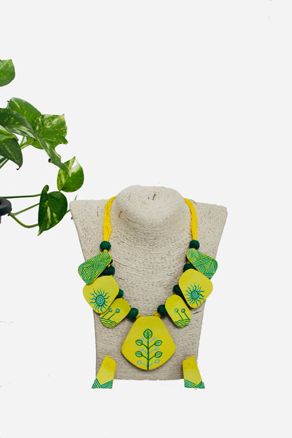 Green and yellow earrings on a beige stand with a plant in the background