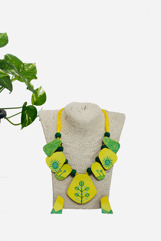 Green and yellow earrings on a beige stand with a plant in the background