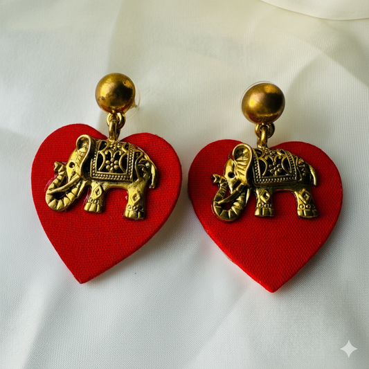 Red heart-shaped earrings with gold elephant designs on a white background