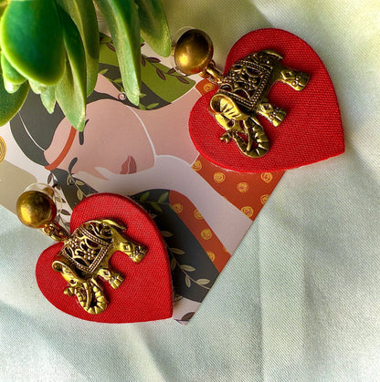 Heart-shaped red fabric clips with gold turtle designs on a white surface with a plant in the corner.