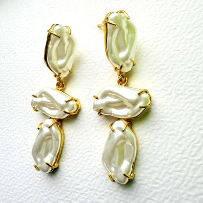 Pair of gold and white earrings on a textured white background