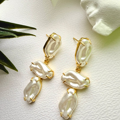 Pearl-like earrings with gold accents on a textured white surface.