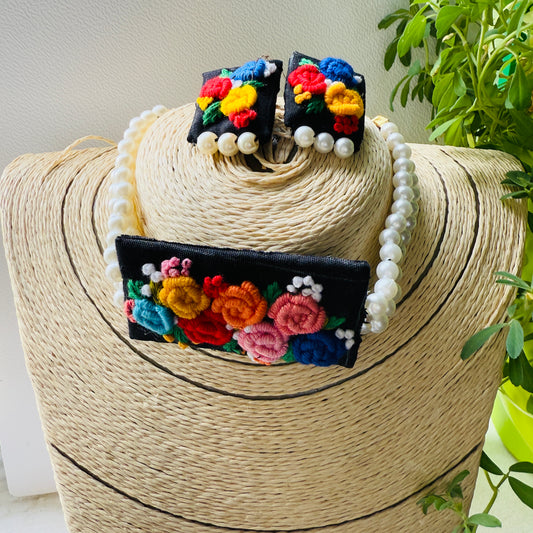 Colorful floral earrings and necklace set on a woven stand with a plant in the background
