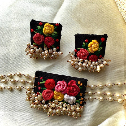 Embroidered floral brooches with pearl accents on a light fabric background