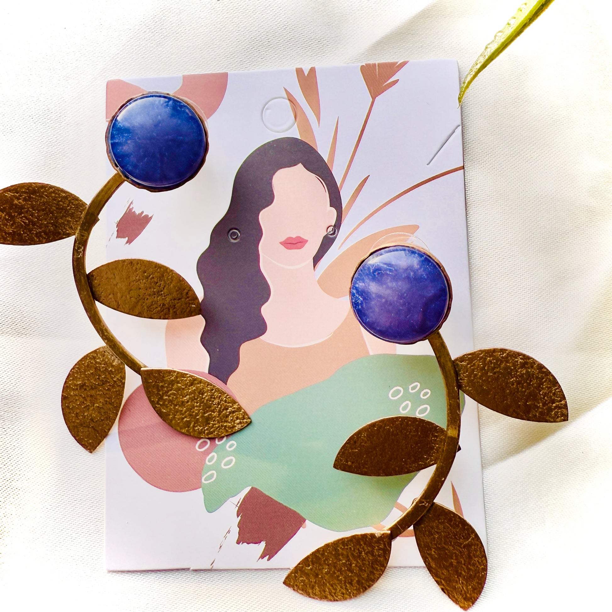 Earrings with blue and gold design on a card with an illustration of a woman.