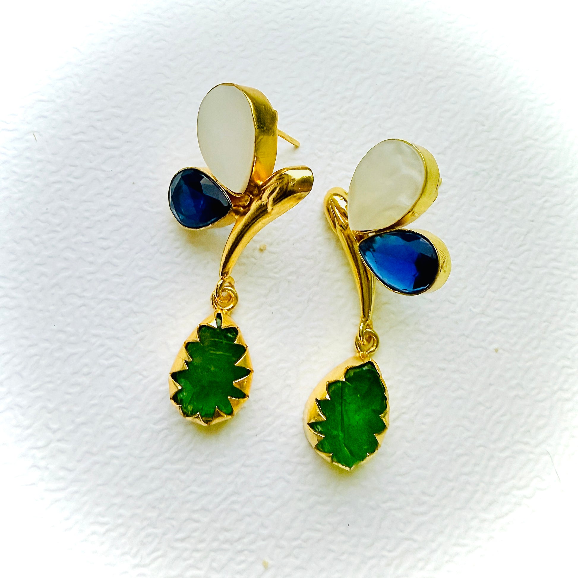 Gold earrings with green and blue gemstones on a white background