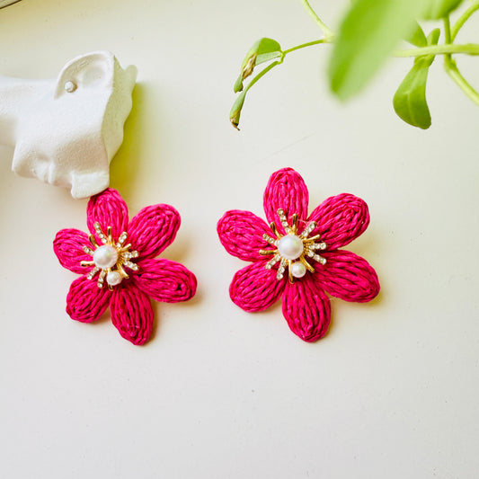 Pink flower-shaped earrings with pearl centers on a white background