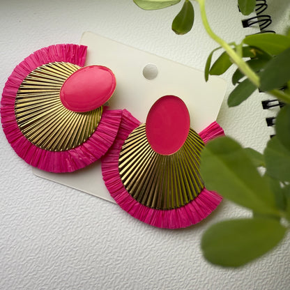Pink and gold earrings on a white background with green leaves.