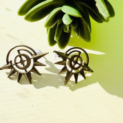 Pair of sun-shaped earrings on a light surface with green leaves in the background