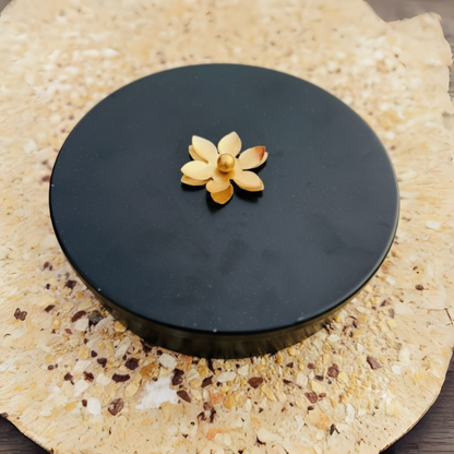 Black round object with a decorative flower on top, placed on a textured beige surface.