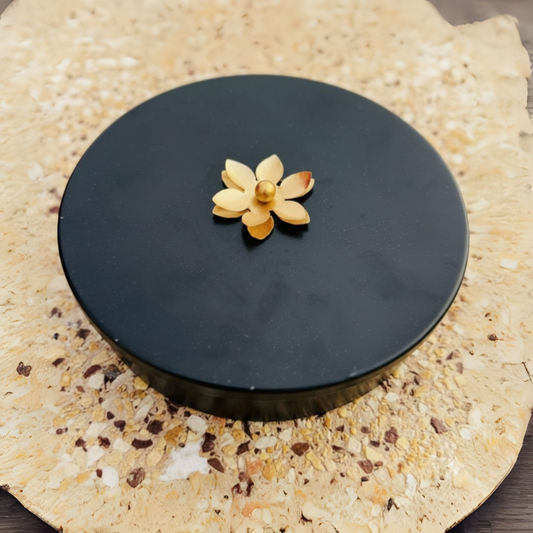 Black round object with a decorative flower on top, placed on a textured beige surface.