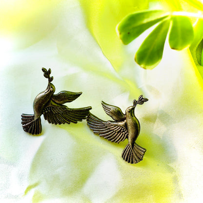 Bronze dove-shaped earrings on a light fabric background with green leaves.