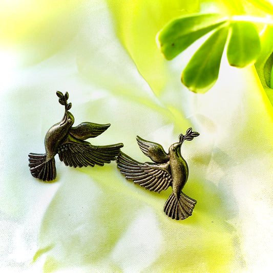 Bronze dove-shaped earrings on a light fabric background with green leaves.