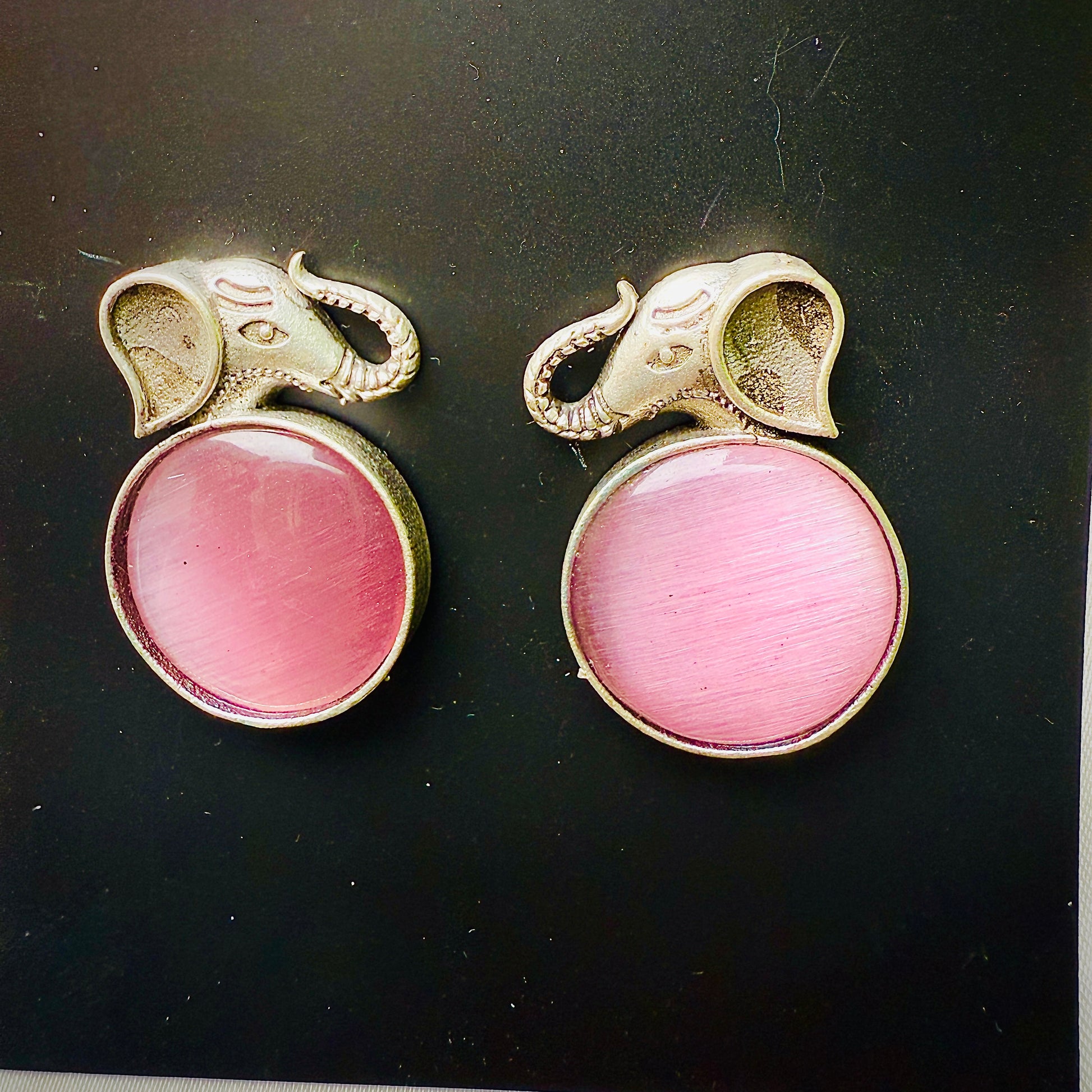 Pair of earrings with pink gemstones and gold elephant designs on a black background