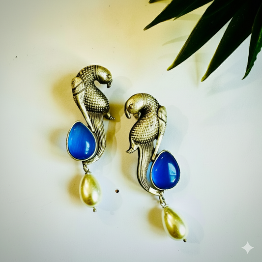 Pair of earrings with parrot design and blue and green stones on a light background