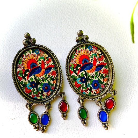 Colorful earrings with floral and bird design on a white background