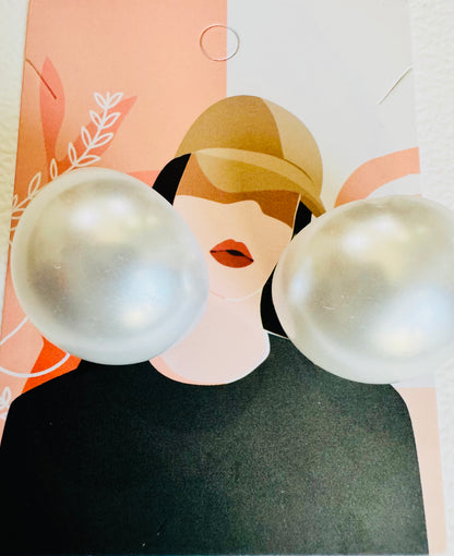 Pearl-like spherical earrings on a card with a stylized face design.