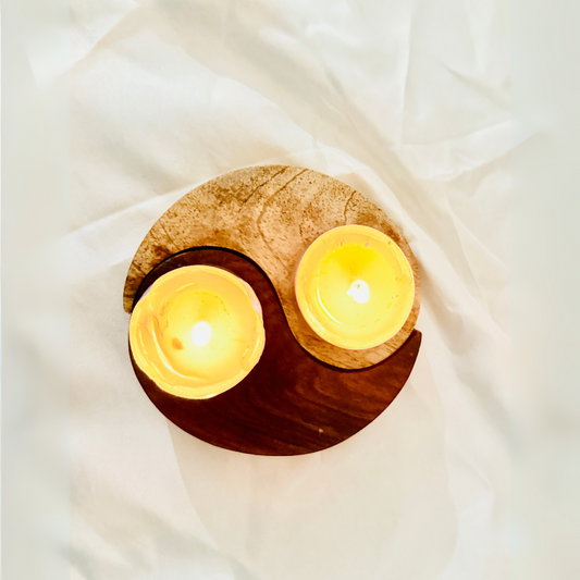 Two lit candles in a wooden yin yang design on a white fabric background
